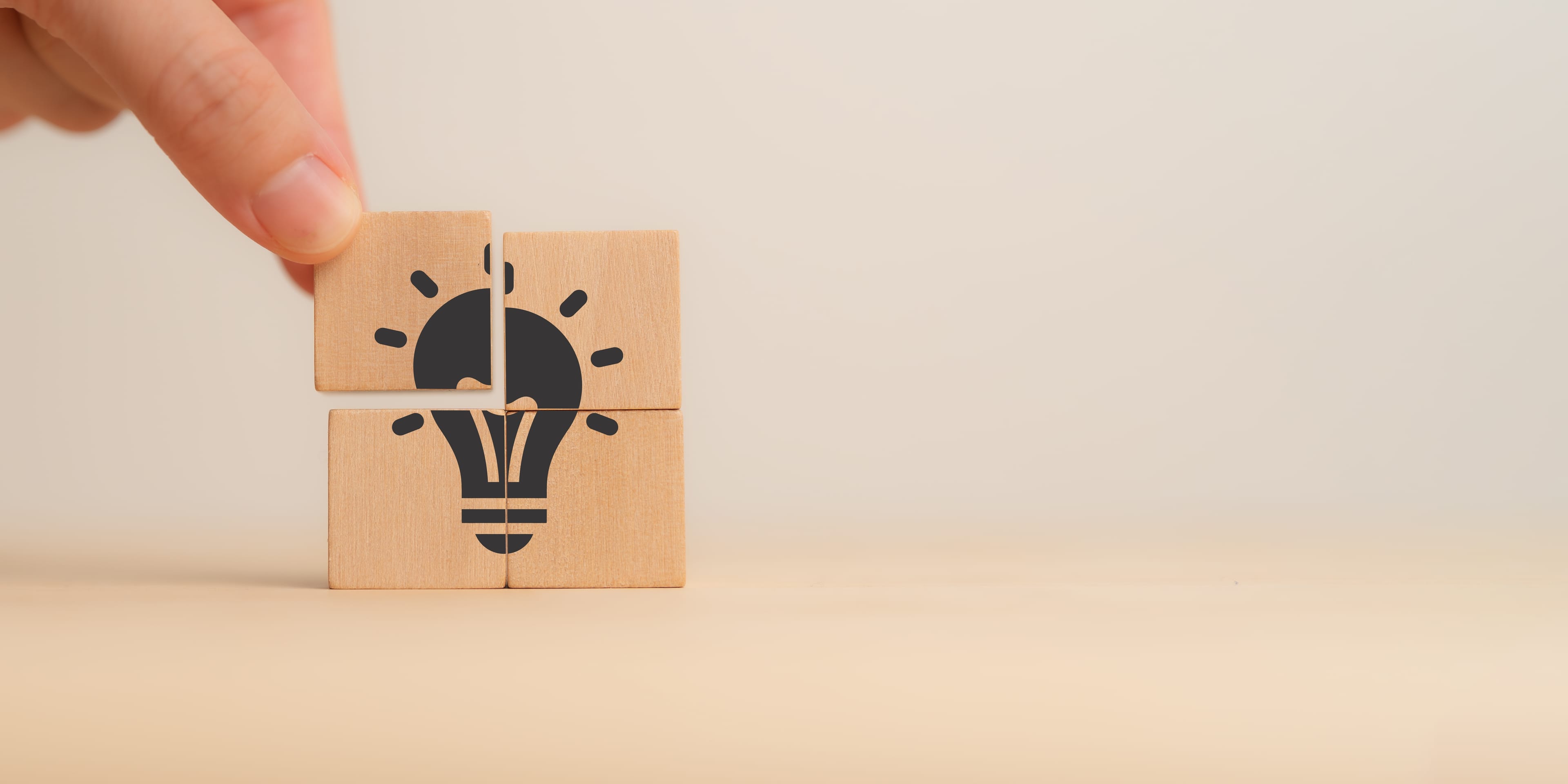 Ideas, creativity, innovation, problem-solving. A close-up of a hand assembling wooden puzzle pieces to form a lightbulb, symbolizing the concept of ideas, creativity, innovation and problem-solving.