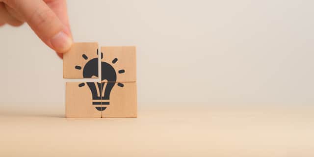 Ideas, creativity, innovation, problem-solving. A close-up of a hand assembling wooden puzzle pieces to form a lightbulb, symbolizing the concept of ideas, creativity, innovation and problem-solving.