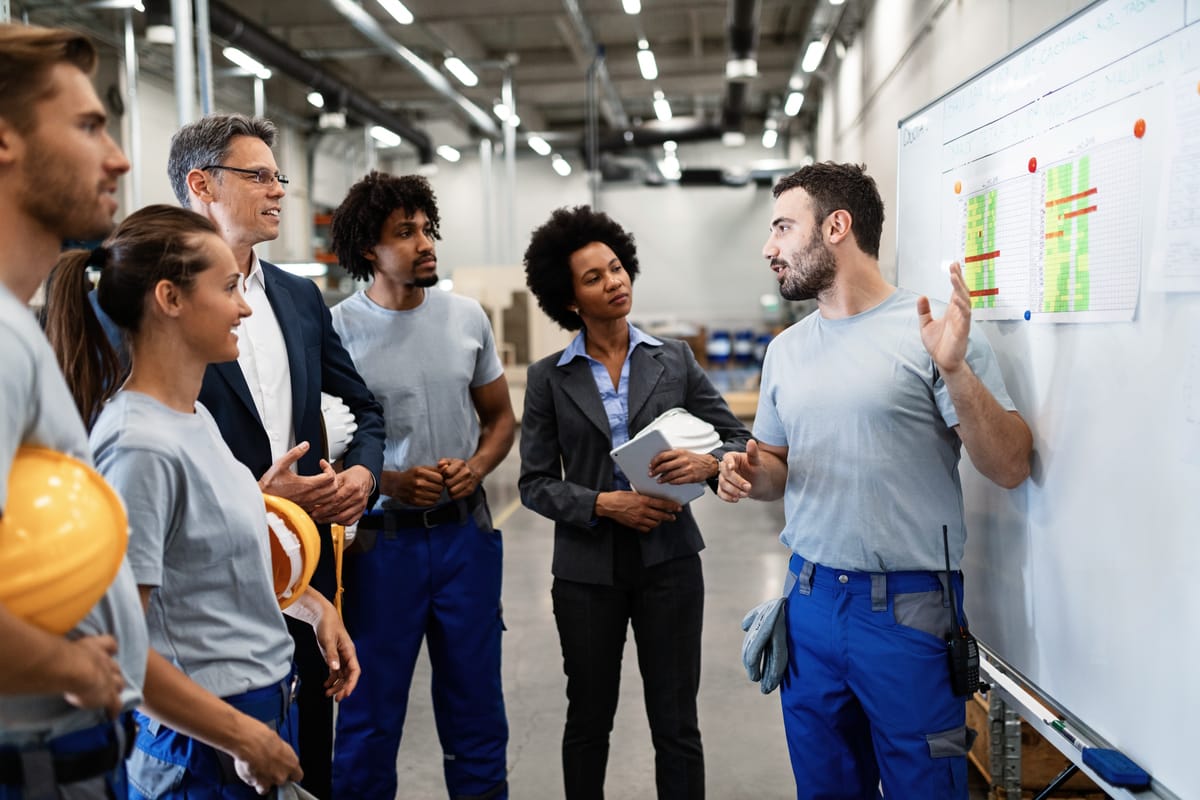 Profissional apresenta dados a uma equipe em ambiente industrial, ilustrando carreira técnica ou liderança.