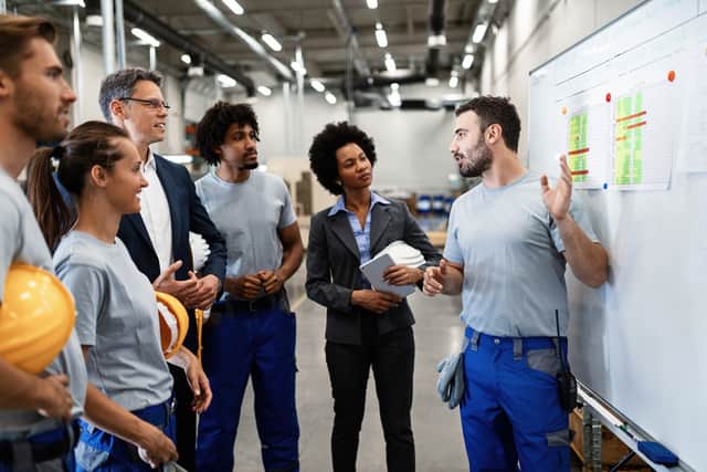 Profissional apresenta dados a uma equipe em ambiente industrial, ilustrando carreira técnica ou liderança.